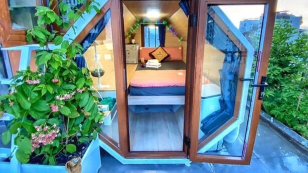 Um quarto compacto e octogonal com uma cama, uma mesinha e uma cadeira.