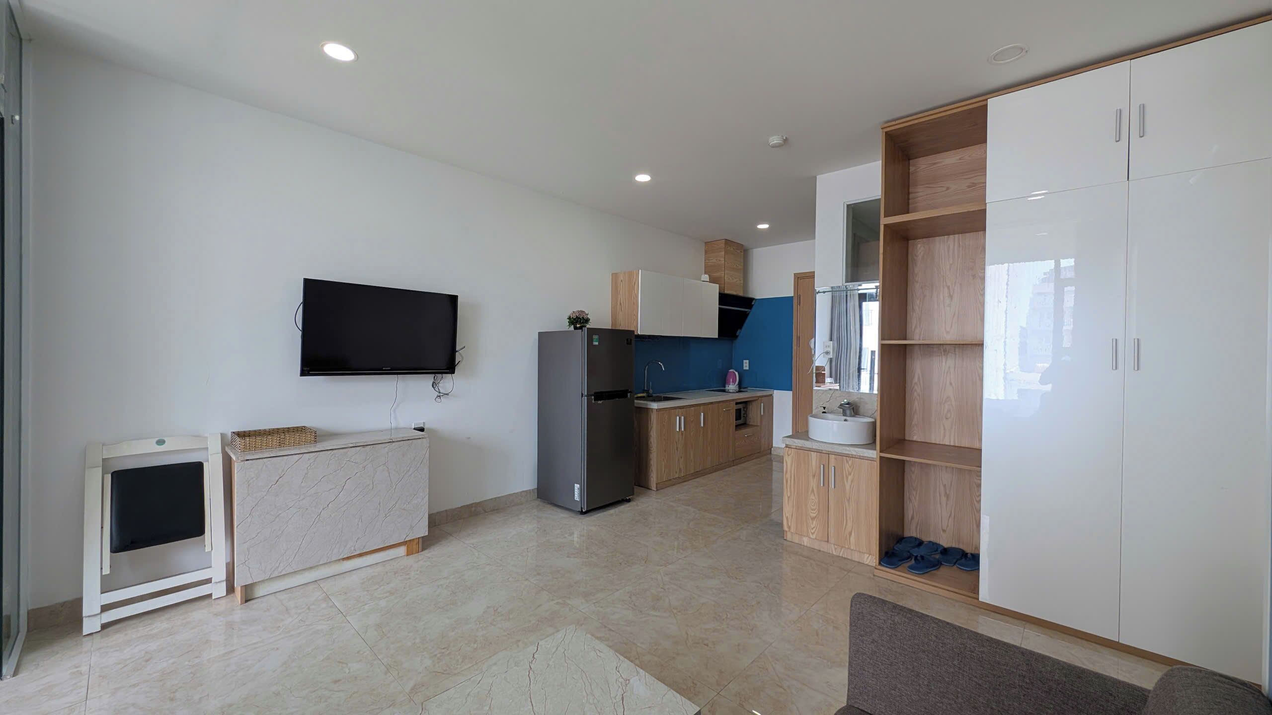 A modern kitchen with a flat-screen TV, a refrigerator, wooden cabinets, and a built-in oven.