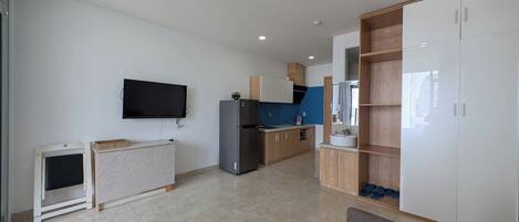 A modern kitchen with a flat-screen TV, a refrigerator, wooden cabinets, and a built-in oven.