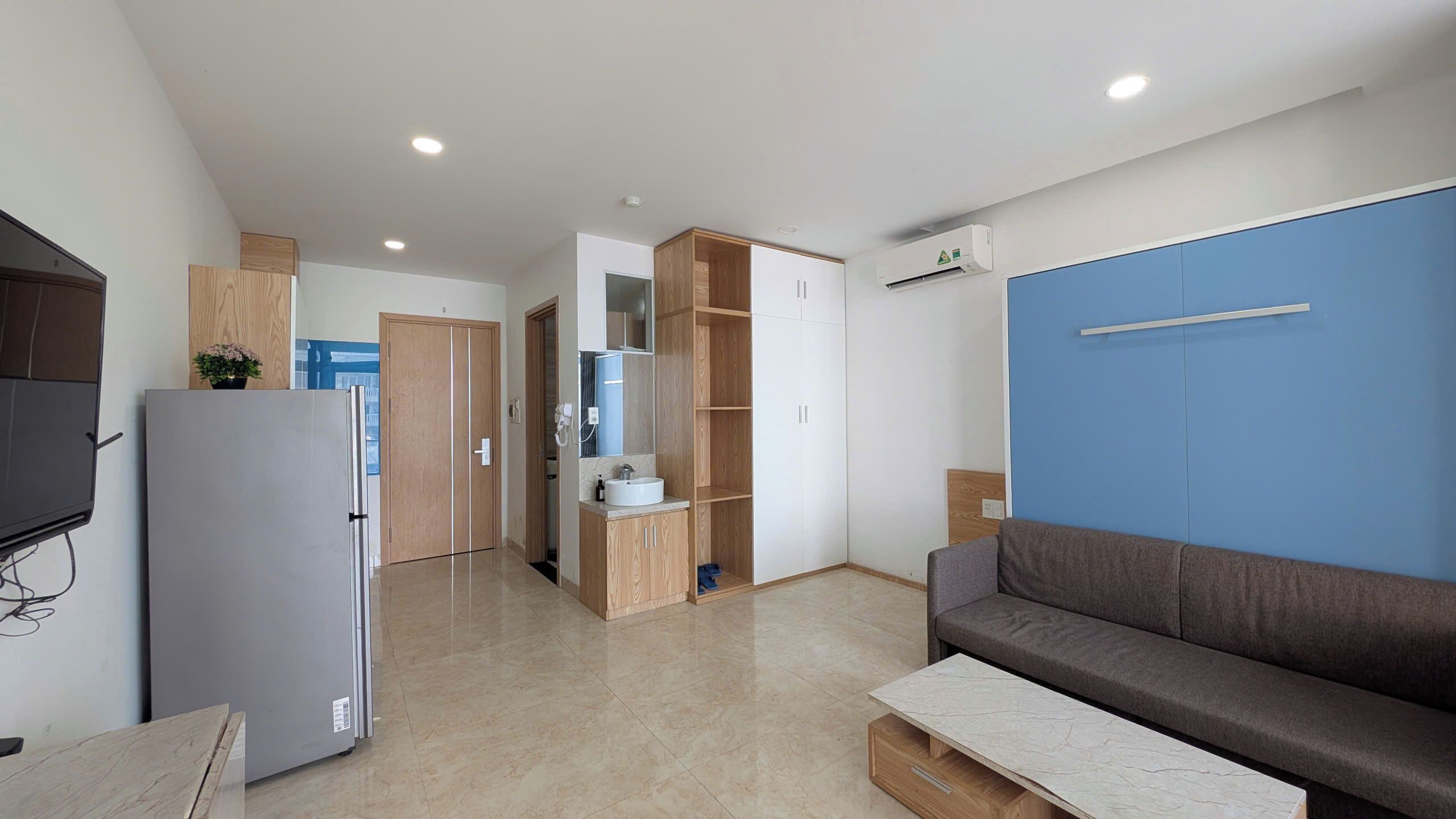 A modern apartment with a kitchenette, a sofa, a dining table, and a blue accent wall.