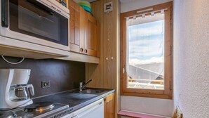 A compact kitchenette with a microwave, coffee maker, and stove. There's a window with a view of a snowy landscape. - 2-room apartment, 4 people, pets allowed, Mont Blanc view (La Plagne-Tarentaise)
