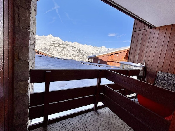 En träbalkong med ett metallräcke som vetter ut mot ett snötäckt berglandskap.