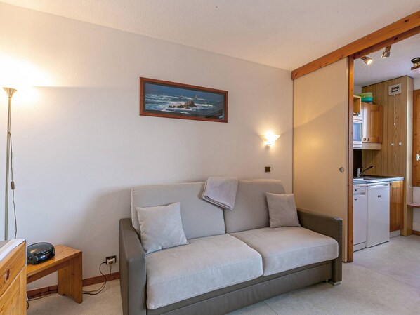 Uma sala de estar acolhedora com um sofá cinzento, uma pequena mesa de madeira e uma pintura de uma paisagem costeira.