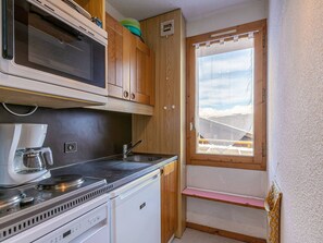 A compact kitchenette with a microwave, coffee maker, and stove. There's a window with a view of a snowy landscape.