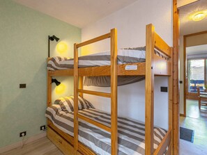 A bunk bed room with a light green wall, wooden frame, and striped bedding.
