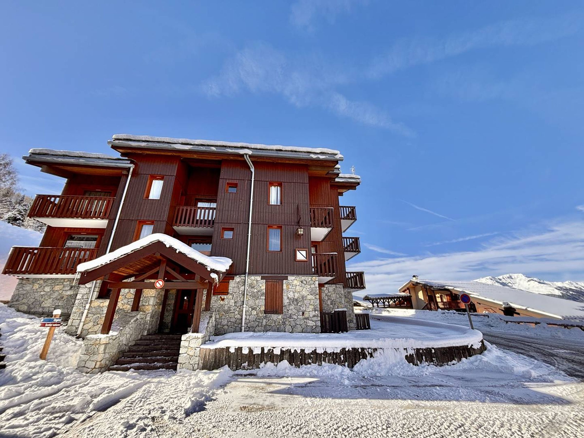 A multi-story wooden chalet with stone foundations, a balcony, and a snow-covered entrance.