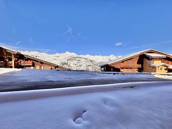 Een berglandschap met sneeuw, houten gebouwen, een heldere lucht en een duidelijke voetafdruk in de sneeuw.
