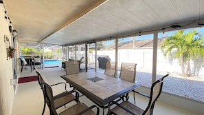 Une terrasse couverte avec une table et des chaises, une piscine et un barbecue.