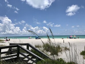 A beach with a wooden staircase leading down to the sand, a clear blue sky, and a few people and umbrellas in the distance. - Sunshine Oasis 2 With Heated Pool.  Minutes to Gulf Beaches and IMG (Bradenton)