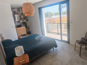 A bedroom with a large bed, a wooden nightstand, a mirror, a hanging light fixture, and a view of the outdoors through a sliding glass door.