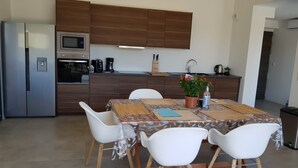 A modern kitchen with a built-in microwave, oven, and coffee maker. There is a dining table with four white chairs and a potted plant. - Villa Rossa, Contemporary Heated pool  (PALASCA)