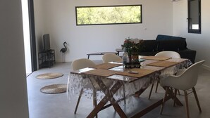 A modern dining area with a table set for four, surrounded by chairs. There is a large window above the table, a potted plant on the table, and a black sofa in the background. - Villa Rossa, Contemporary Heated pool  (PALASCA)