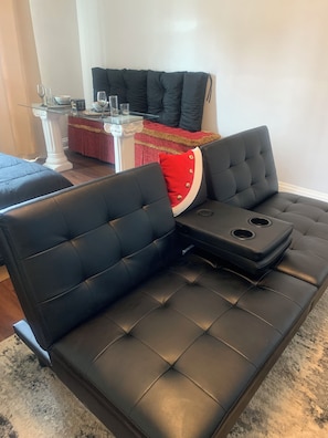 A black leather sofa with a red accent pillow, a glass coffee table, and a white side table with a decorative bowl.
