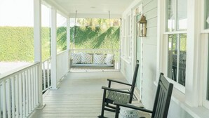 A covered porch with white railings, wooden benches, and a view of a green landscape.