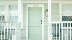 A two-story house with a light green door marked 1055, white railings, and a small porch area.