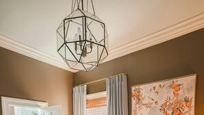 A bedroom with a bed, a geometric chandelier, a shower, and a door leading to a bathroom.
