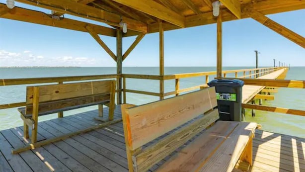 A wooden pier with benches and a trash can, overlooking a calm body of water. - Come on down for a great fishing and beach get away at Benjamin's Pier! (Rockport)