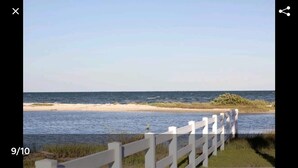 A coastal scene with a white fence, a sandy beach, and a calm sea under a clear sky. - Come on down for a great fishing and beach get away at Benjamin's Pier! (Rockport)