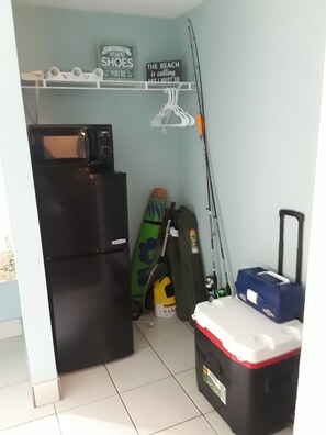 A compact kitchen with a refrigerator, microwave, and a small countertop. There are storage items like a cooler and a bag on the floor. - Come on down for a great fishing and beach get away at Benjamin's Pier! (Rockport)