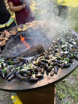A large outdoor grill with seafood, including mussels, and a fire burning in the center.
