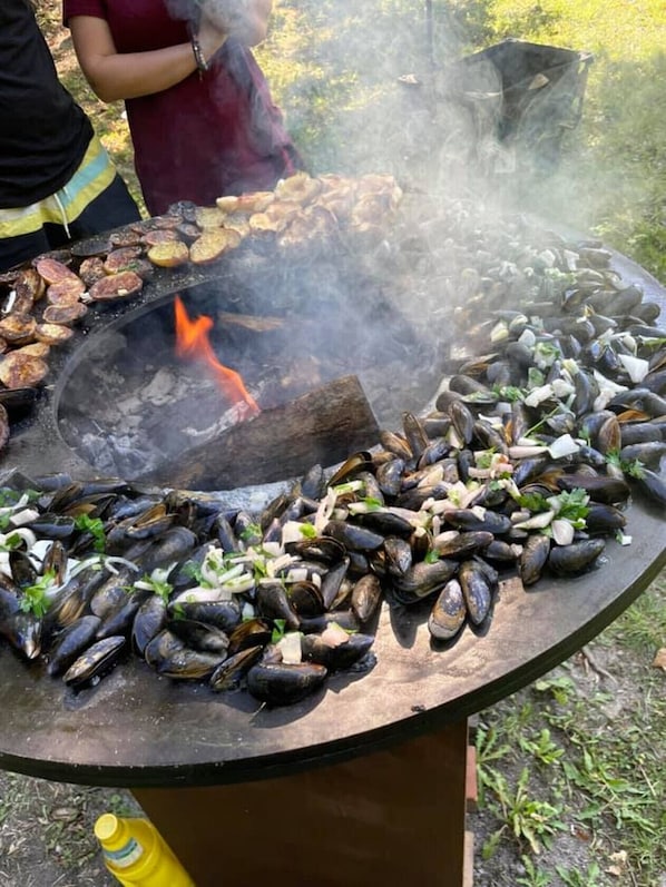 Una grande griglia all'aperto con pesce, tra cui cozze, e un fuoco acceso al centro.