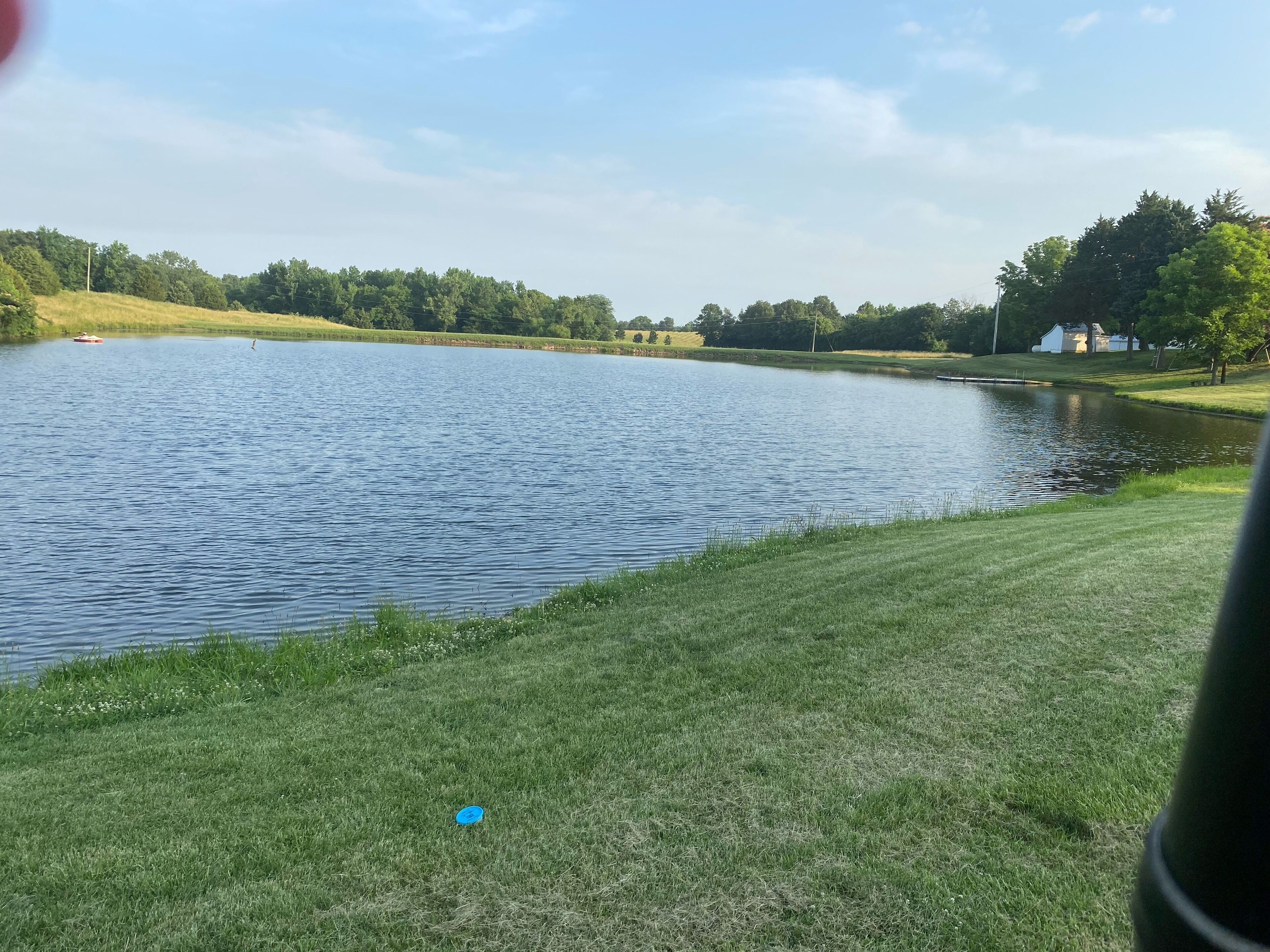 Um lago calmo com margens gramadas e árvores ao fundo.
