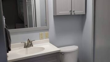 Une salle de bain avec un lavabo blanc, un miroir et des placards, des toilettes et une porte.