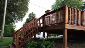 Une terrasse en bois avec un escalier menant à une zone abritée, entourée de pelouse et d’arbres.