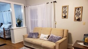 Un salon avec un canapé beige, deux coussins, un tapis gris à motifs et une petite table sur laquelle est posé un objet décoratif.