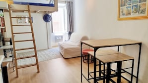 A room with a bunk bed, a desk with a chair, a small table, a white couch, and a framed picture on the wall.