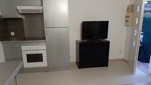A compact kitchen with a refrigerator, oven, and a small black TV stand. - F2, air conditioned all comfort (Fréjus)