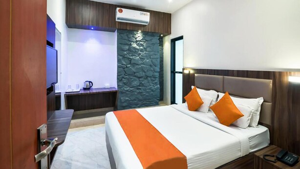A hotel room with a bed, a desk, a television, a coffee machine, and a stone wall. - Hotel Sea Grand (Mumbai)