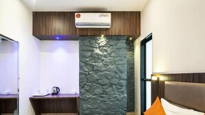 A hotel room with a bed, a nightstand, a stone accent wall, an air conditioning unit, and a window. - Hotel Sea Grand (Mumbai)