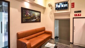 A reception area with a brown leather sofa, a framed painting, a television mounted on the wall, and a sign indicating payment upon check-in. - Hotel Sea Grand (Mumbai)
