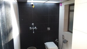 A small, enclosed bathroom with a toilet, a shower, and a sink. - Hotel Sea Grand (Mumbai)