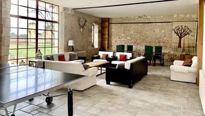 A spacious living area with a ping pong table, multiple sofas, and a stone wall.