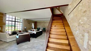 A spacious living area with a wooden staircase, stone walls, and large windows.