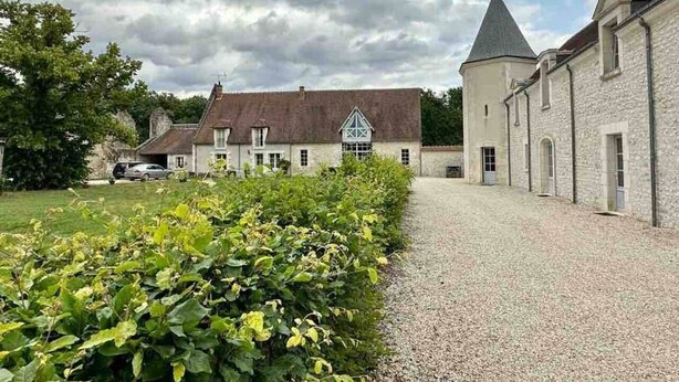 A building with a gravel driveway, a hedge, and a car parked in the background.
