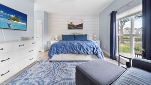 Quarto com cama, televisão, ventilador de teto, janela com cortinas e vista para o exterior.