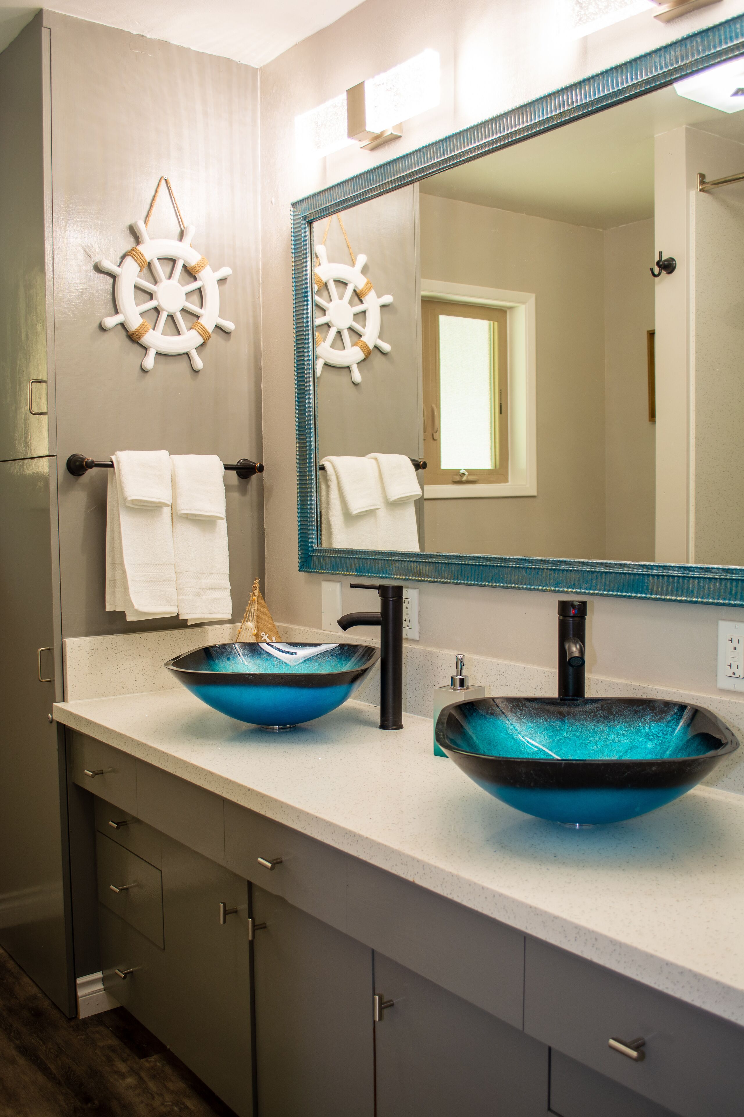A bathroom with two sinks, a large mirror, and decorative ship wheel wall art.
