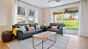 Ein modernes Wohnzimmer mit einer schwarzen Ledersofa, einem Holztisch und Blick auf einen üppigen Garten durch große Schiebeglasüren.