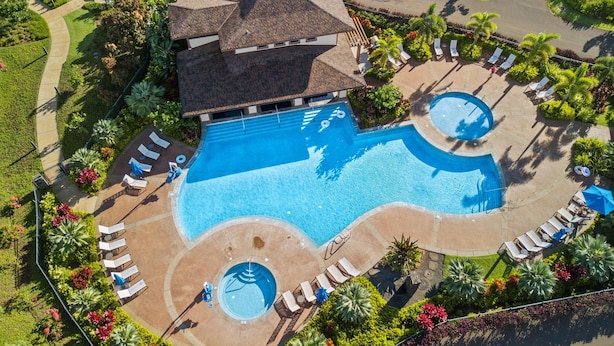 Eine Vogelperspektive zeigt ein Resort mit einem großen, zentralen Pool, mehreren kleinen Rundpools und zahlreichen Liegebereichen mit Sonnenliegen.
