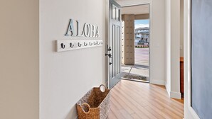 Ein Flur mit einem 'ALOHA' Schild, einem Korb und einer Tür, die nach draußen führt.