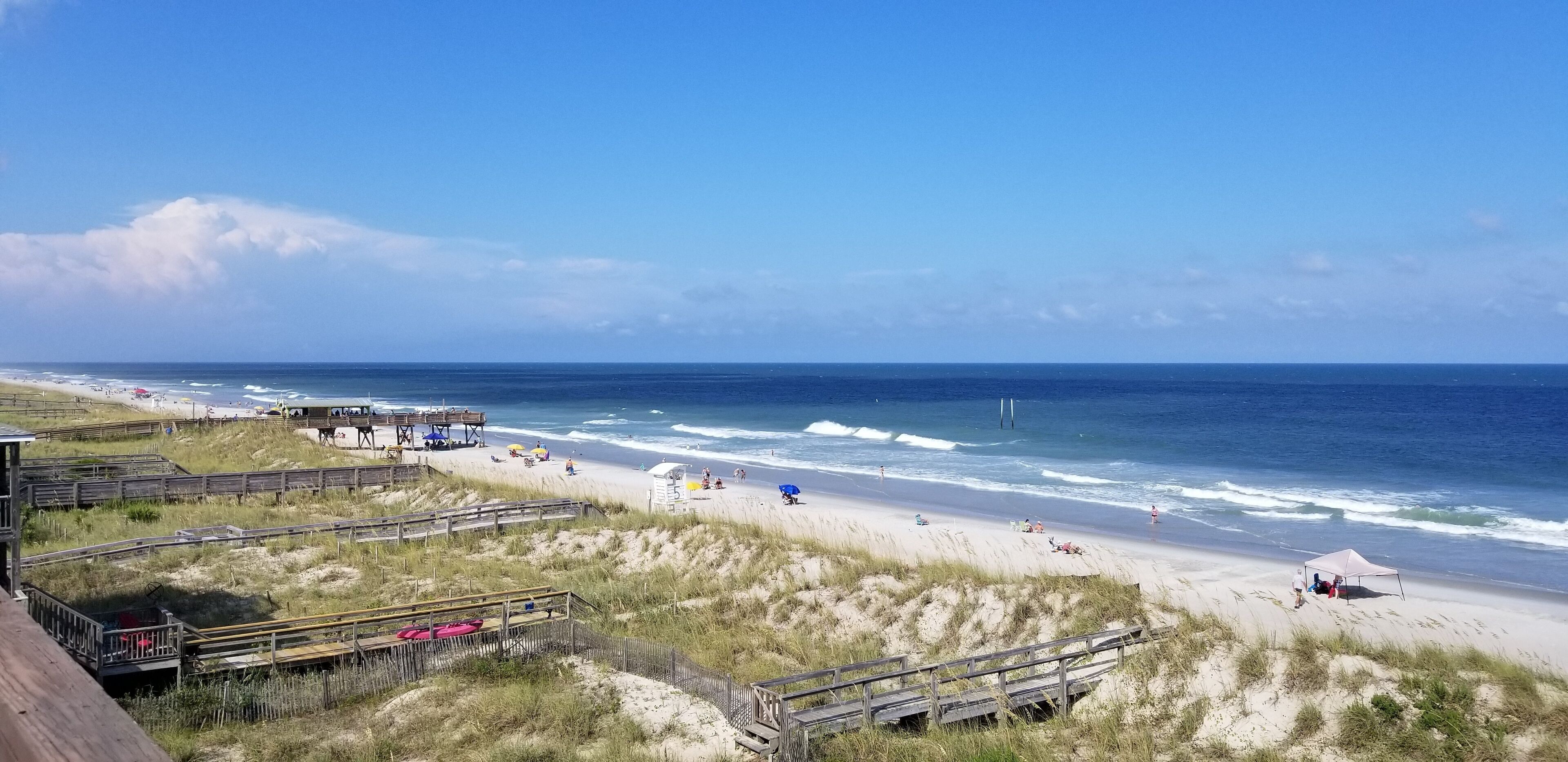 A beach with wooden walkways, a lifeguard tower, and beach umbrellas.