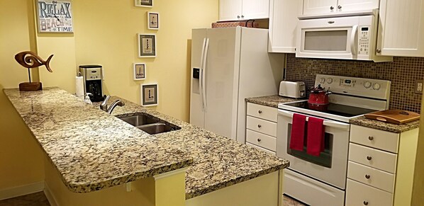 A kitchen with granite countertops, a refrigerator, a microwave, a stove, and a sink. - Beautiful oceanfront 2 bedroom, 2 bath condo with elevator, pool and huge deck. (Carolina Beach)