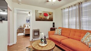 Un salon avec un canapé, un ventilateur de plafond, un tableau et une fenêtre avec des rideaux.