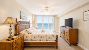 A bedroom with a bed, a dresser, a television, a ceiling fan, and a view of the ocean through large windows. - Oceanfront | Heated Pool-Towers Grande #508 (Daytona Beach Shores)