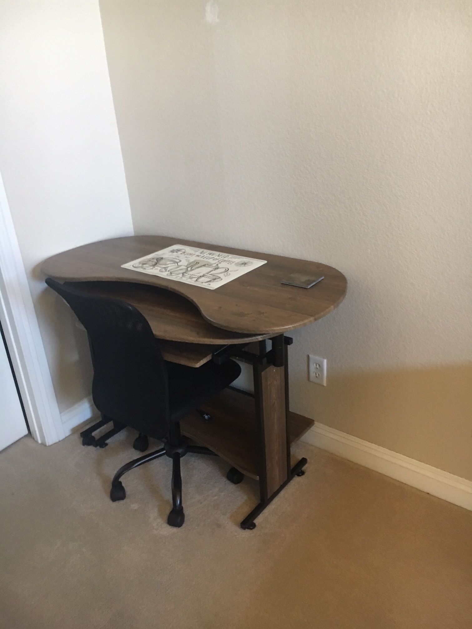 Ein Schreibtisch im Eckbereich mit einem Stuhl, einem kleinen Regal und einem Schild darauf.