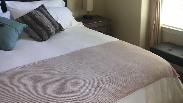 Una cama bien hecha con un cojín a rayas, un cuadro floral enmarcado en la pared y una mesita de noche con una lámpara.
