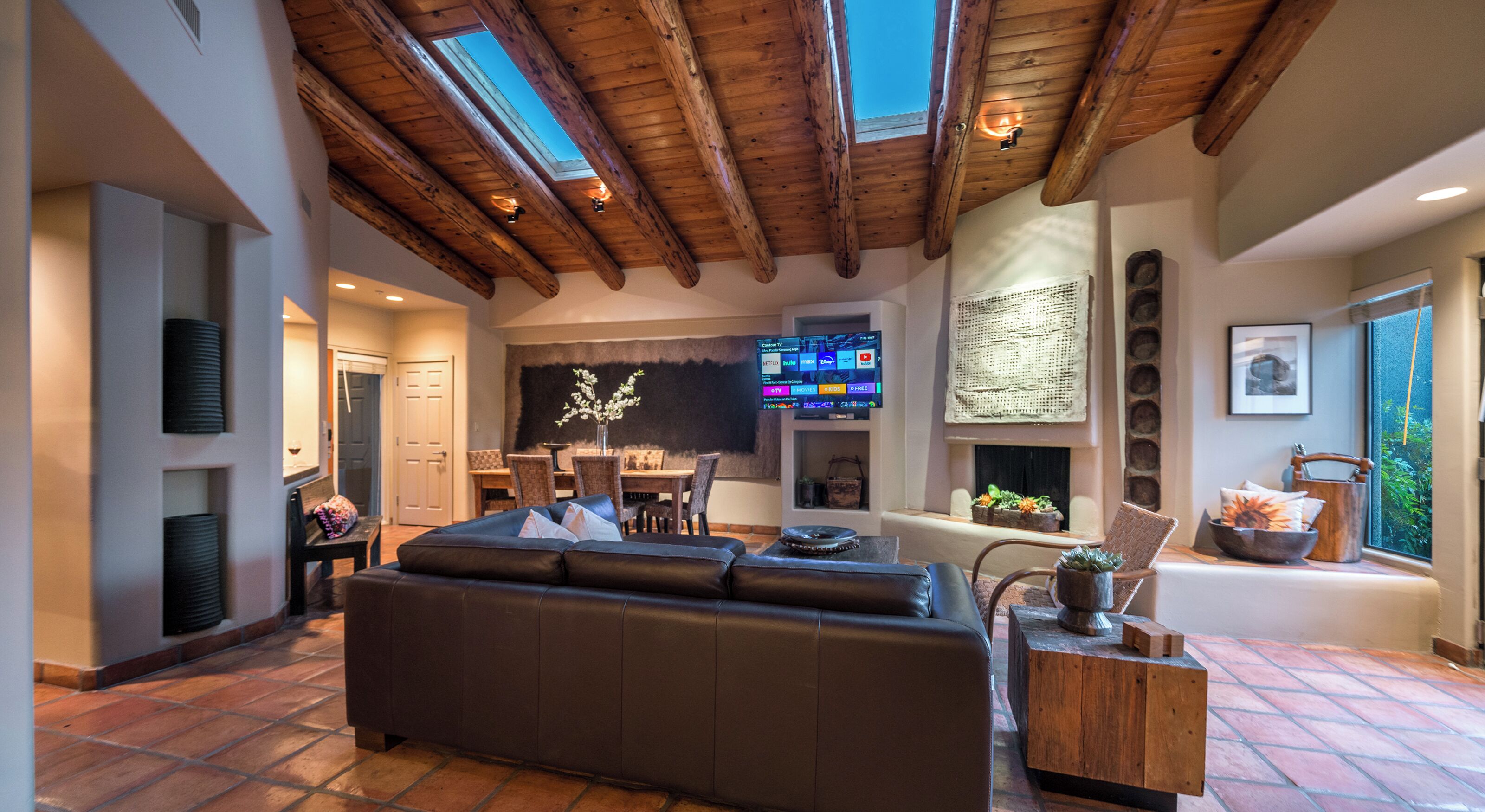 A spacious living area with a high ceiling and skylights, a comfortable sofa, a dining area, and a fireplace.
